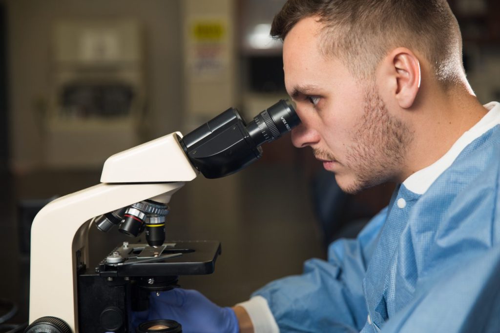 A medical lab technician student looks into a microscope