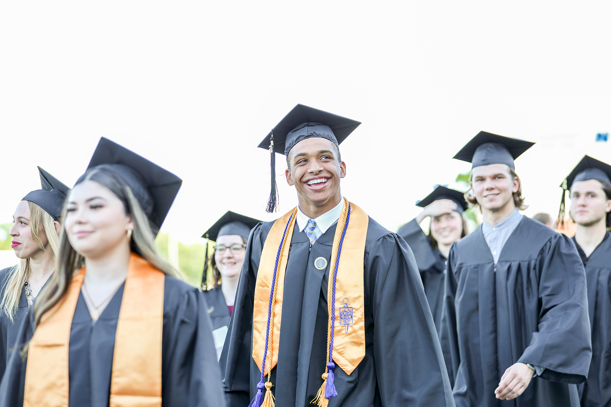 Graduate in cap and gown smiles while walking in a group.