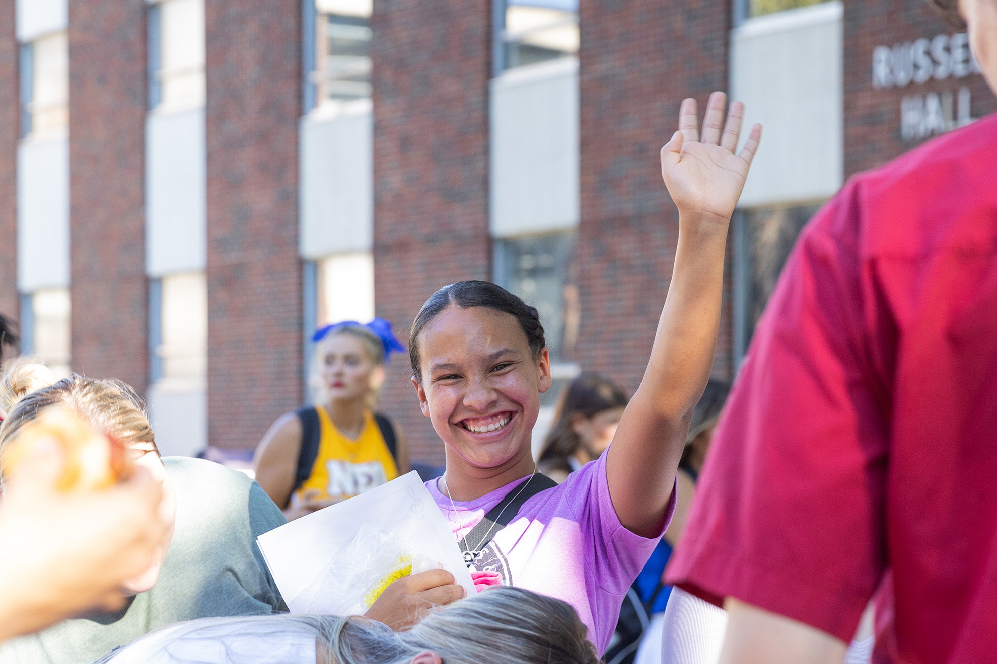 College student standing in a crowd smiles and waves