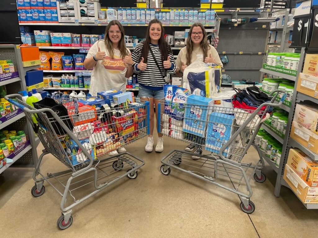 A group of volunteers pose proudly behind their service work of donated food items in grocery baskets in a grocery aisle.